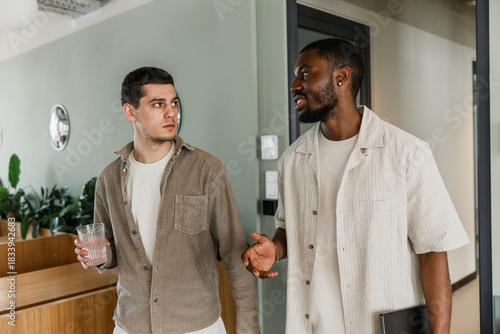 A male worker is holding a glass and listening to a male worker talking to him