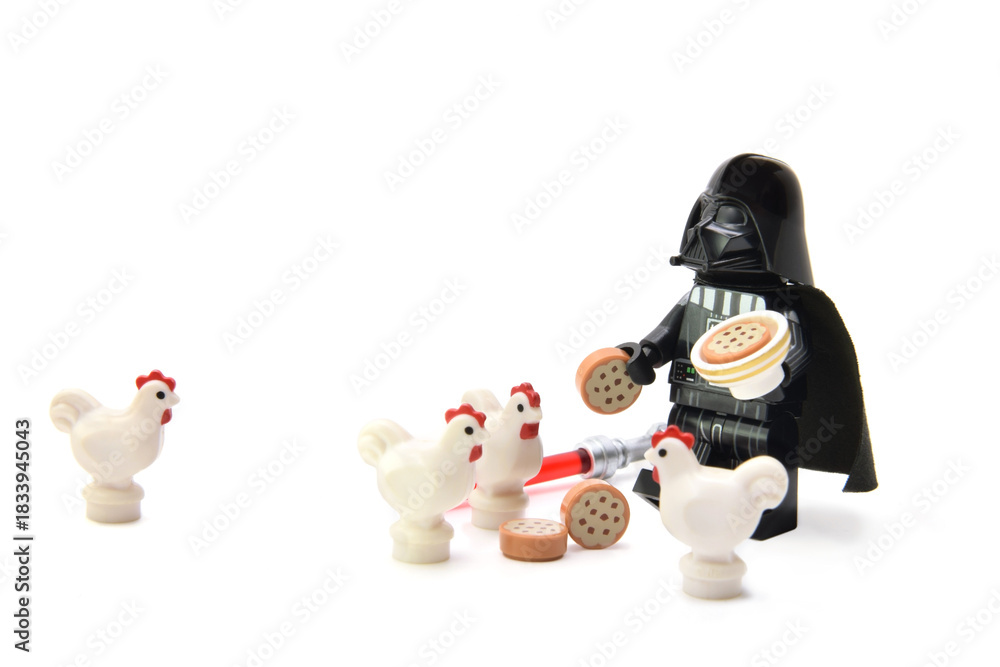 Fototapeta premium Lego minifigure of peaceful Darth Vader from Star Wars is feeding the chicken isolated on white. Editorial illustrative image of stop war concept.