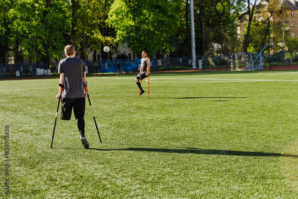 Obraz premium Male player watches ball in front of male player catching it while they lean on crutches