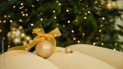 Golden Christmas ball on a light sofa on a blurred Christmas tree with lights