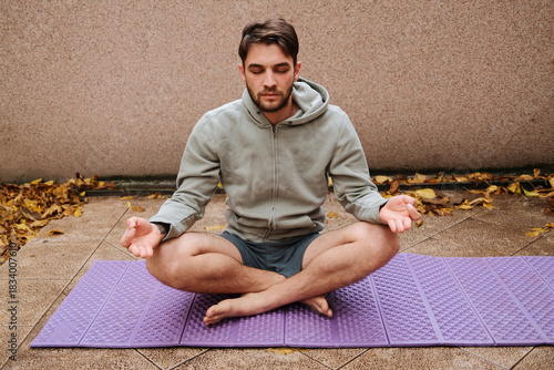 A man sits cross-legged meditating on a purple mat. The calm moment highlights mindfulness and balance.