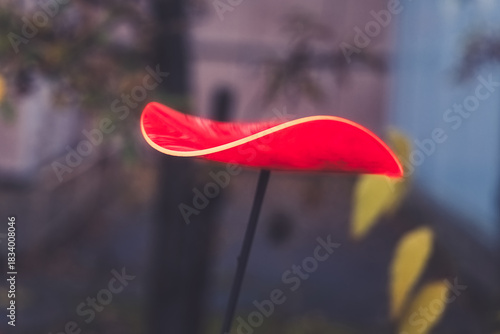 Colorful red sculpture stands tall in a serene urban garden surrounded by faintly blurred yellow leaves on a bright autumn day
