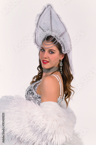 Model in a silver sequin dress, white fluffy wrap and beaded kokoshnik poses elegantly in a studio, showcasing a refined stage-inspired look