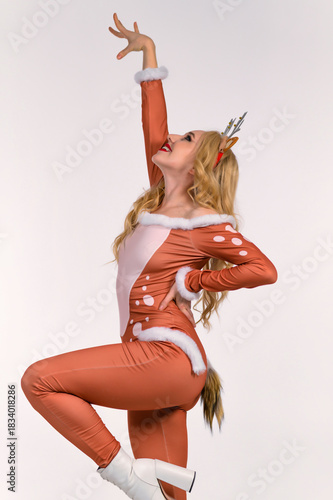 Elegant woman in a festive doe costume with antler headband, soft fur trim and tail posing in a dynamic dance stance against a clean studio background, perfect for holiday creative projects