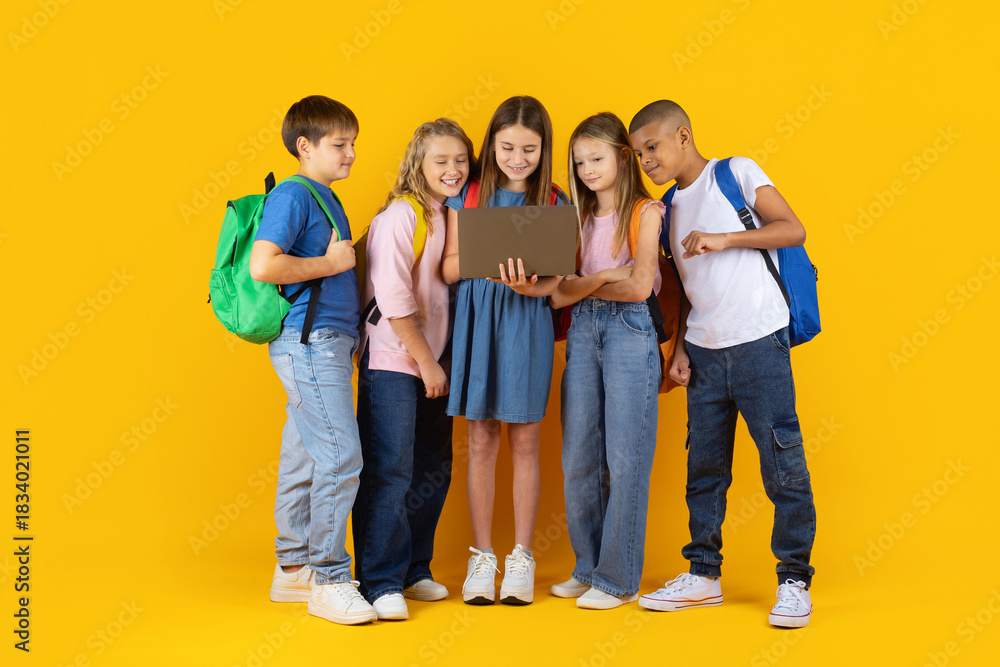 Fototapeta premium Group of preteen children gathered around a laptop in a bright studio background. Curious pupils exploring digital learning together in a modern education lifestyle scene