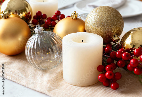 Christmas table setting with gold baubles and white candle. Festive holiday decoration with red berries and glass ornament