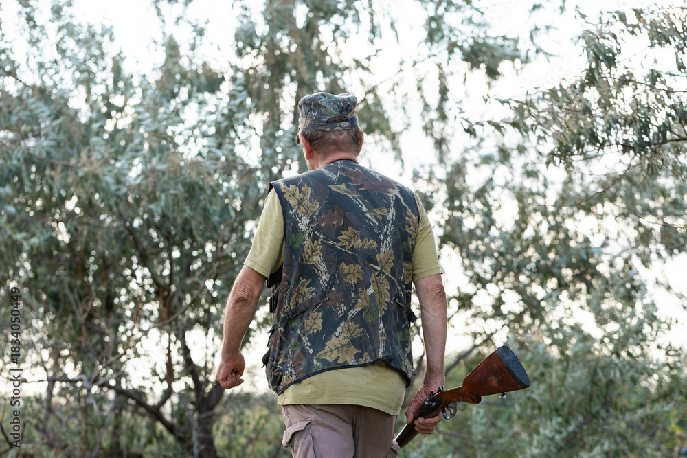 Fototapeta premium A hunter with a gun in camouflage clothing. A gentleman with a gun, medium shot, unrecognizable.