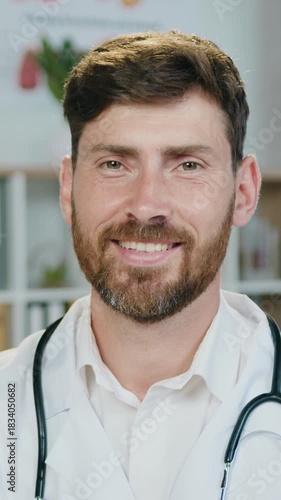 Handsome in high spirits successful experienced friendly bearded medical worker in white coat with stethoscope around his neck posing on camera with sincerely smile ,front view