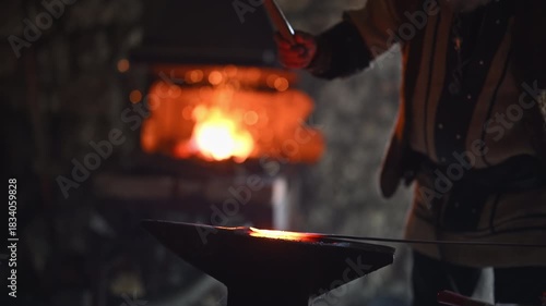 A Viking blacksmith with a white beard and braided hair works intently at a forge, hammering glowing metal on an anvil, with flames flickering in the background of a stone workshop cinematic slow