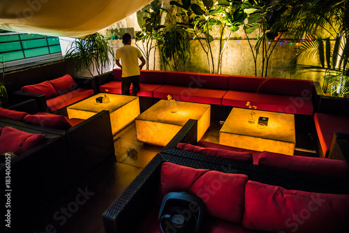 A cozy lounge with wicker sofas and glowing tables, surrounded by plants and warm lighting.