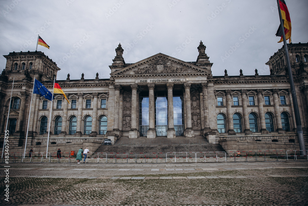 Obraz premium The historic Reichstag building in Berlin adorned with German and European flags.