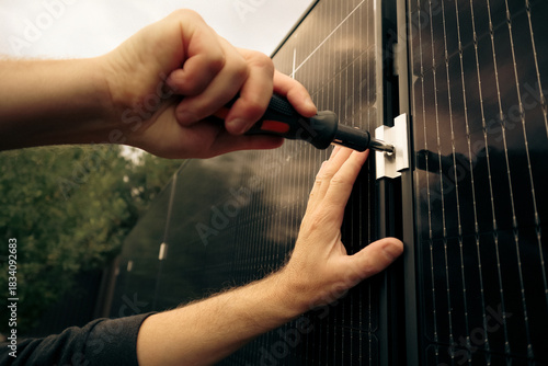 Worker tightening screws on a solar panel bracket with a screwdriver.