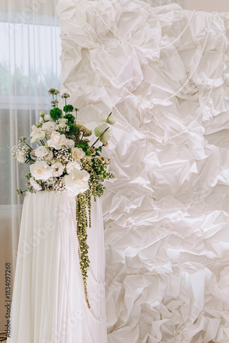 Elegant floral arrangement with white roses and green accents on draped fabric background.