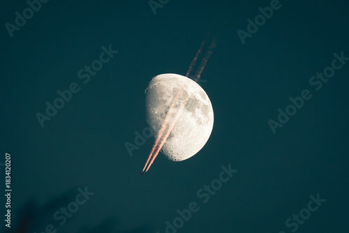 Avion de passage devant la lune, avec trainée de condensation au crépuscule