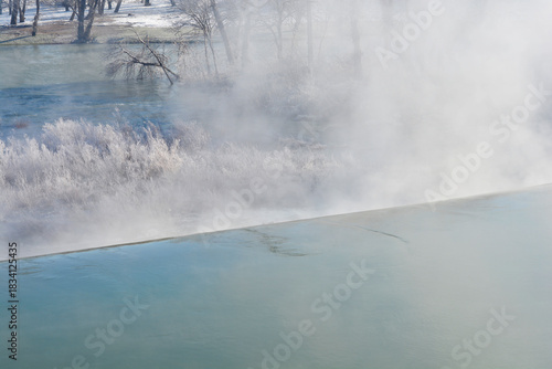 Fototapeta Naklejka Na Ścianę i Meble -  A close-up winter scene of the dam on the Kupa River showing thick river mist rising off the warm water over the weir and heavily frosted bank vegetation