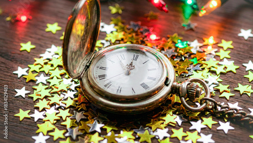 Photography Vintage pocket watch surrounded by gold and silver star confetti and colorful festive string lights, symbolizing New Year's Eve countdown and celebration