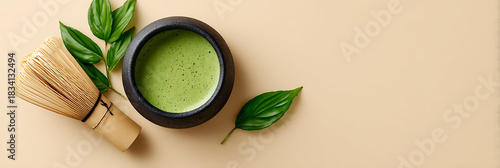 Top view of traditional Japanese matcha tea preparation setup with a black bowl, bamboo whisk, and green tea powder on a beige background.