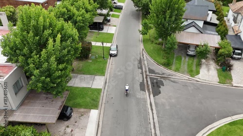 Male cyclist training exercising outdoor. Aerial view, drone following, tracking shot. Cyclist riding a Gravel / Road Bike city / neighborhood / street bike path. Cyclist white cycling jersey.
