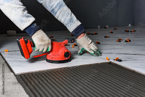 Tiler laying tiles on wall using electric vibrating suction cup.