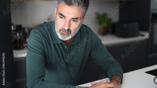 Foto Mature man thinking seriously with concern in kitchen