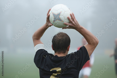 Player performs a throw-in during a soccer match in foggy weather on a grass field in the early morning