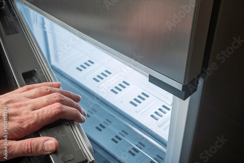 Male hand on open freezer door, inspection of clean empty drawers, concept of home appliance maintenance, repair, food safety control