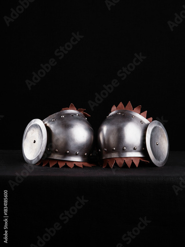 Matching steel shoulder pauldrons with rondel discs and decorative leather edging, set against a dark background for dramatic contrast.