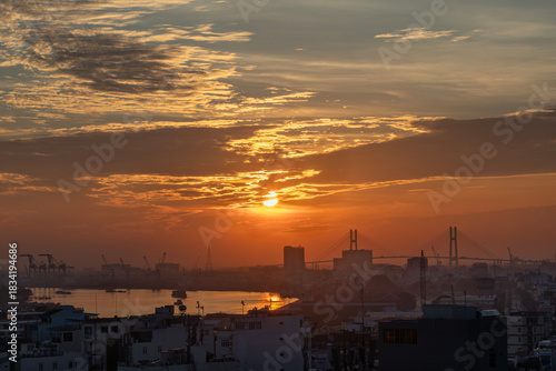 Saigon River Sunrise looking toward port and Phu My Bridge with shipping on the water and beautiful red sky.