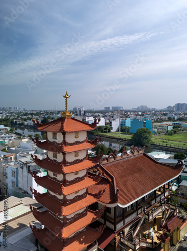Vertical wide drone view over Buddhist pagoda in busy urban area of Ho Chi Minh City, Vietnam on a sunny clear day featuring roof decoration and the transportation infrastructure
