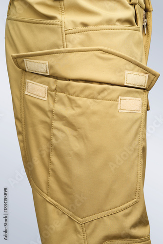A detailed view of a khaki-colored pants pocket showcasing intricate stitching and closure design, ideal for illustrating themes of utility and textile craftsmanship.