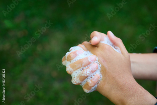 Two hands are rubbing together with soap bubbles while standing outdoors in a green garden. This activity showcases the importance of hygiene and cleanliness.