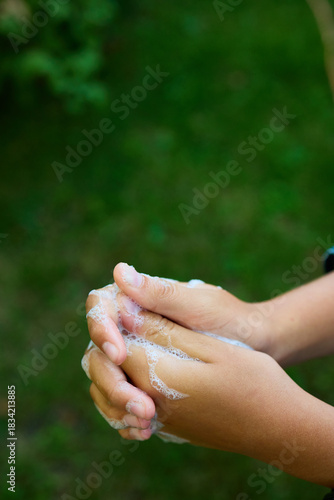Two hands are rubbing together with soap bubbles while standing outdoors in a green garden. This activity showcases the importance of hygiene and cleanliness.