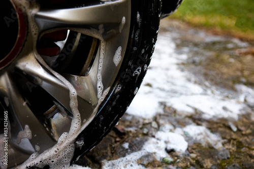 Fotografija Cleaning car wheel with soap and water in a backyard during a sunny afternoon The suds are visible on the shiny rim