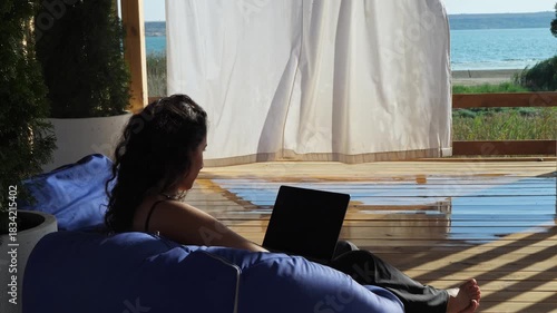A woman relaxing and working on her laptop on a beautiful, breezy patio