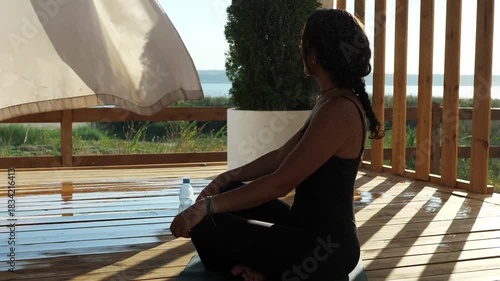 A woman sitting peacefully on her yoga mat, enjoying the view from a breezy patio
