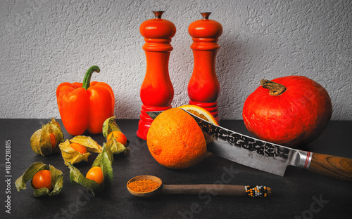 A pumkin, orange pepper belle, physalis fruits on a slate countertop