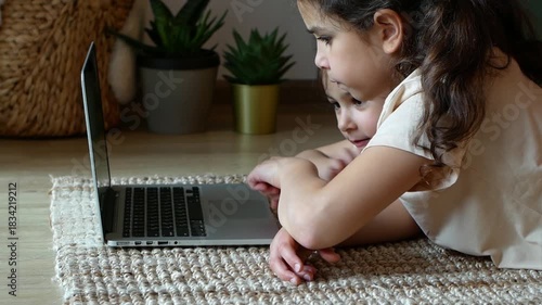 Two young sisters learning and playing together on a laptop