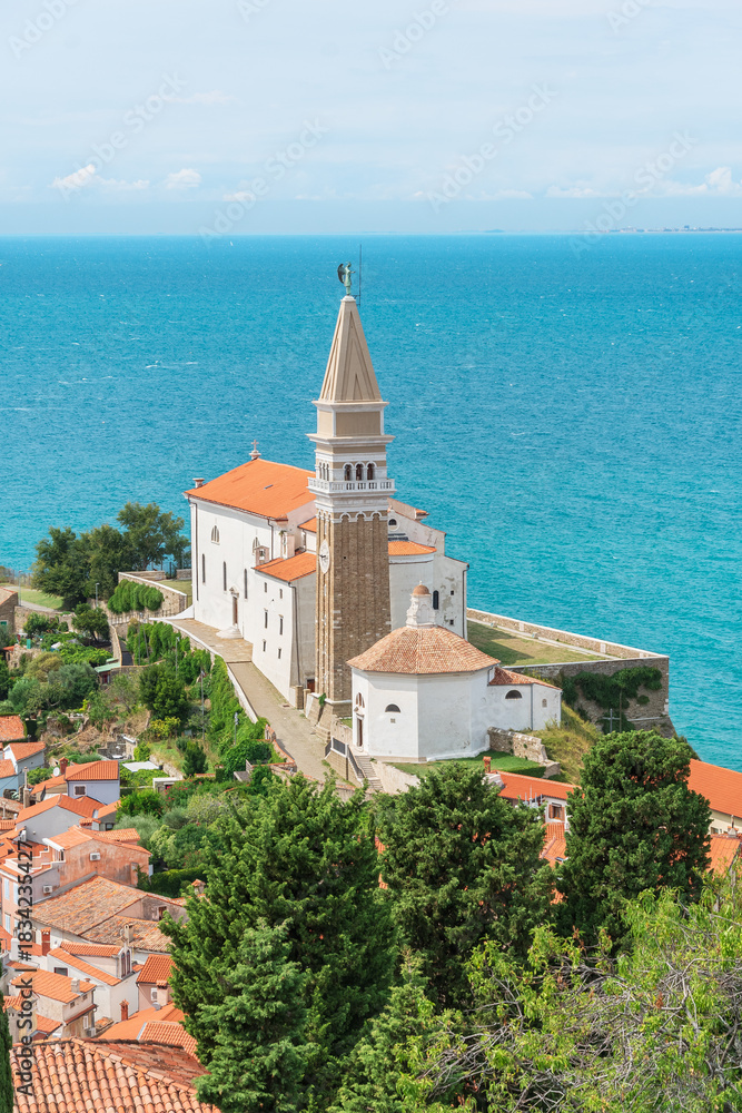 Obraz premium The coastal town of Piran in Slovenia, with the Church of St. George towering over the town, the landscape along the seashore, and the view from the Walls of Piran tourist attraction.