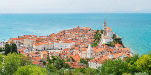 The coastal town of Piran in Slovenia, a picturesque seaside landscape, seen from the Walls of Piran tourist attraction. Colorful buildings surrounded by blue water.