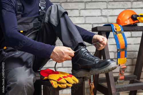 Construction worker putting protective boots, yellow gloves and hard hat.