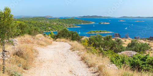 Croatian coastal landscape with small islands in the sea, green forest and blue water, view from a gravel bike path on a hill on a sunny day.