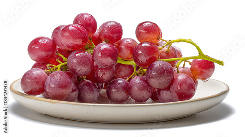 A bunch of red grapes with water droplets on a white plate against a white background close up