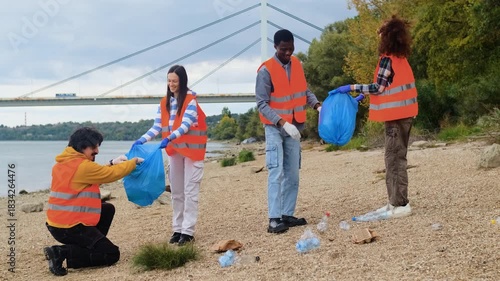 Smiling volunteers collecting garbage in blue bags during riverbank cleanup.