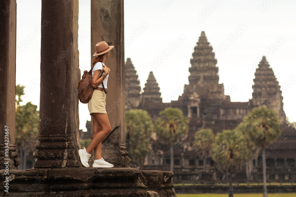 Naklejka premium Female Tourist Exploring Ancient Temple Angkor Wat in Cambodia at Sunrise