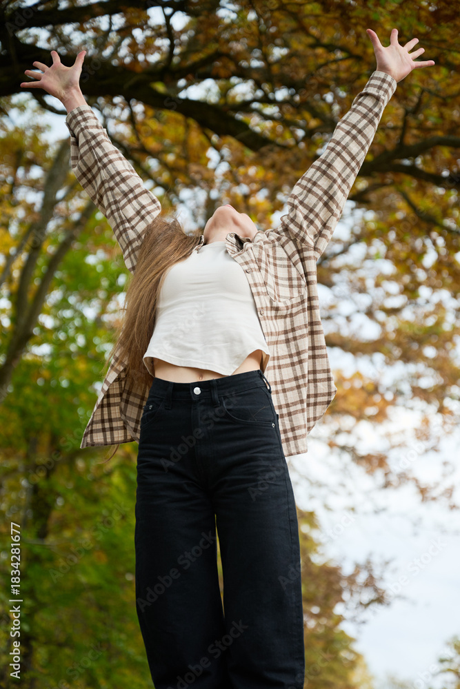 Naklejka premium A person relishes the beauty of fall, arms raised high in excitement. Surrounded by vibrant autumn foliage, the scene radiates joy and freedom.