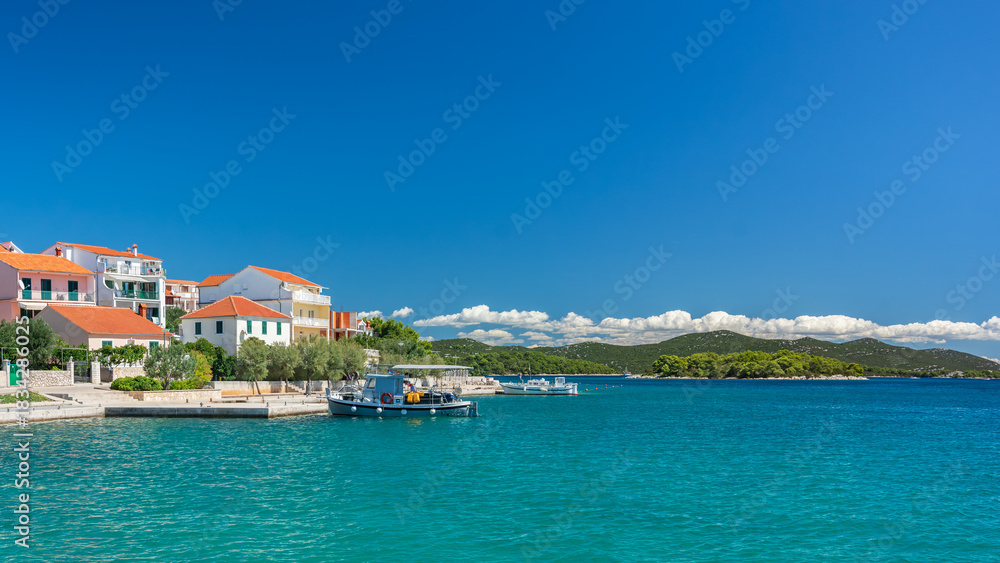 Obraz premium The seaside town of Jezera in Croatia, a small bay with hills above the blue water, view from the bay over the water on a sunny summer day.