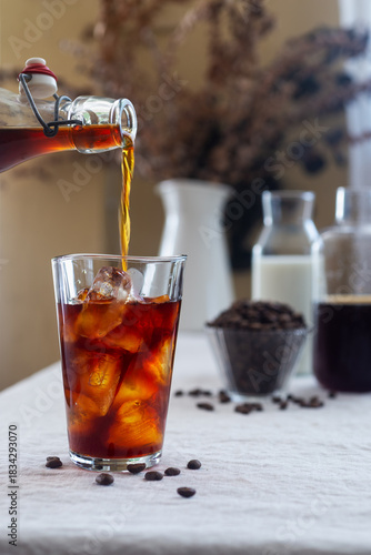 Cold brew coffee is being poured from a bottle into a glass with ice