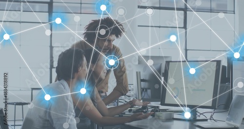 Working three coworkers in casual tops leaning in office, pointing at monitors and network overlay