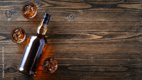 Whiskey Bottle with Glasses and Ice on Rustic Wooden Background, Copy Space