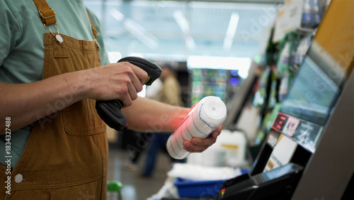 Buyer scanning various items at a self-checkout kiosk in a modern hardware store, utilizing a handheld barcode scanner for efficient and contactless payment